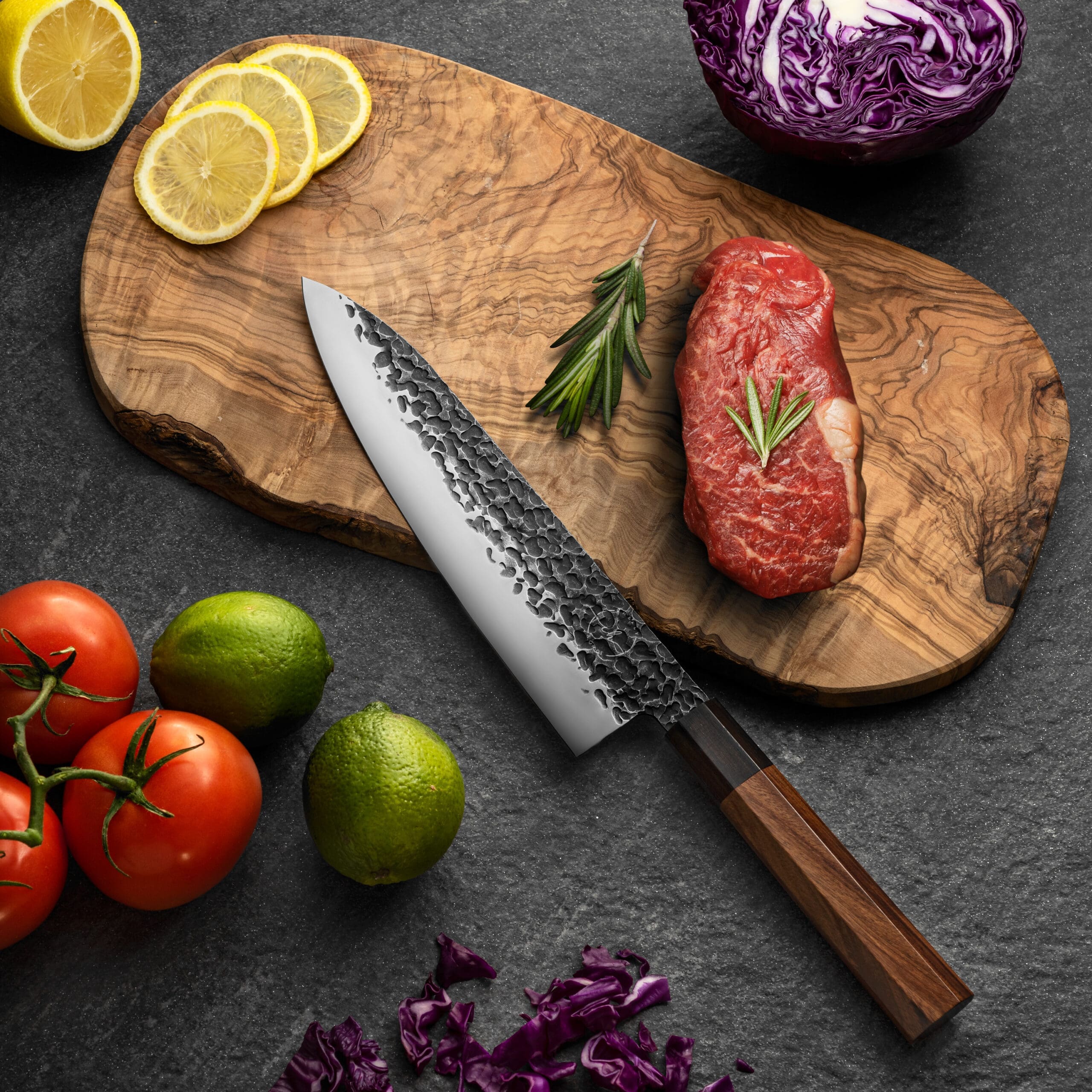 A chef's knife on a cutting board with meat and produce